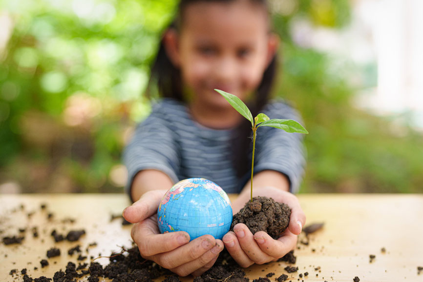 Hier ist ein Mädchen zu sehen , welches in der einen Hand einen Ball als Weltkugel und in der anderen Hand eine kleine grüne Pflanze mit Erde. Dies ist ein Beispielbild für das Rahmenleitbild für Umwelt, Ökologie und Nachhaltigkeit