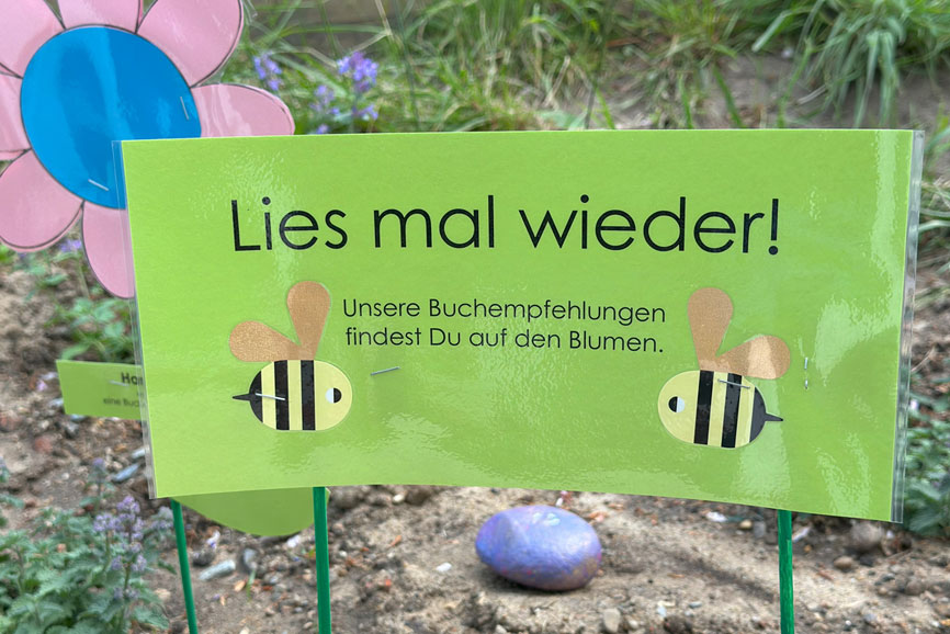 Lies mal wieder steht hier als selbst gebasteltes grünes Schild in einem Blumenbeet - Katholische Schule Maria Grün eröffnet neuen Lesegarten