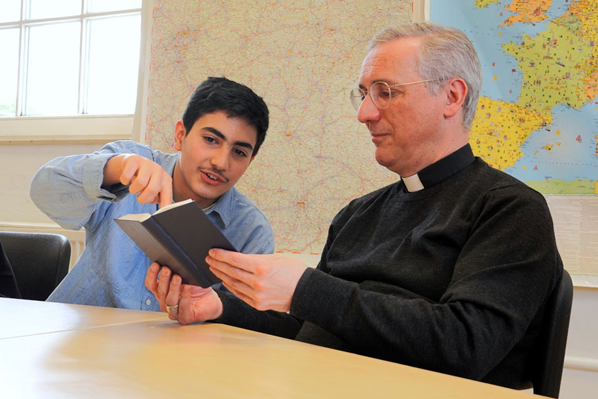 Erzbischof Heße besucht Vorbereitungsklasse für junge Geflüchtete an der Katholischen Schule Harburg. Hier ist er zu sehen mit einem 14-jährigen Iraner. Gemeinsam schauen sie in ein Buch.