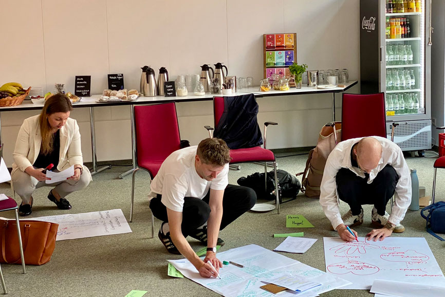 Führungsfreude-Workshop - hier sieht man drei TeilnehmerInnen in der Hocke jeweils vor einem großen Blatt Papier auf dem sie etwas zeichnen.