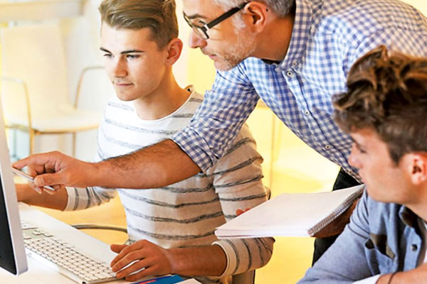 Kirche macht Schule Kurs 9 - hier sieht man einen Mann, der zwei Jugendlichen etwas am Computer erklärt.